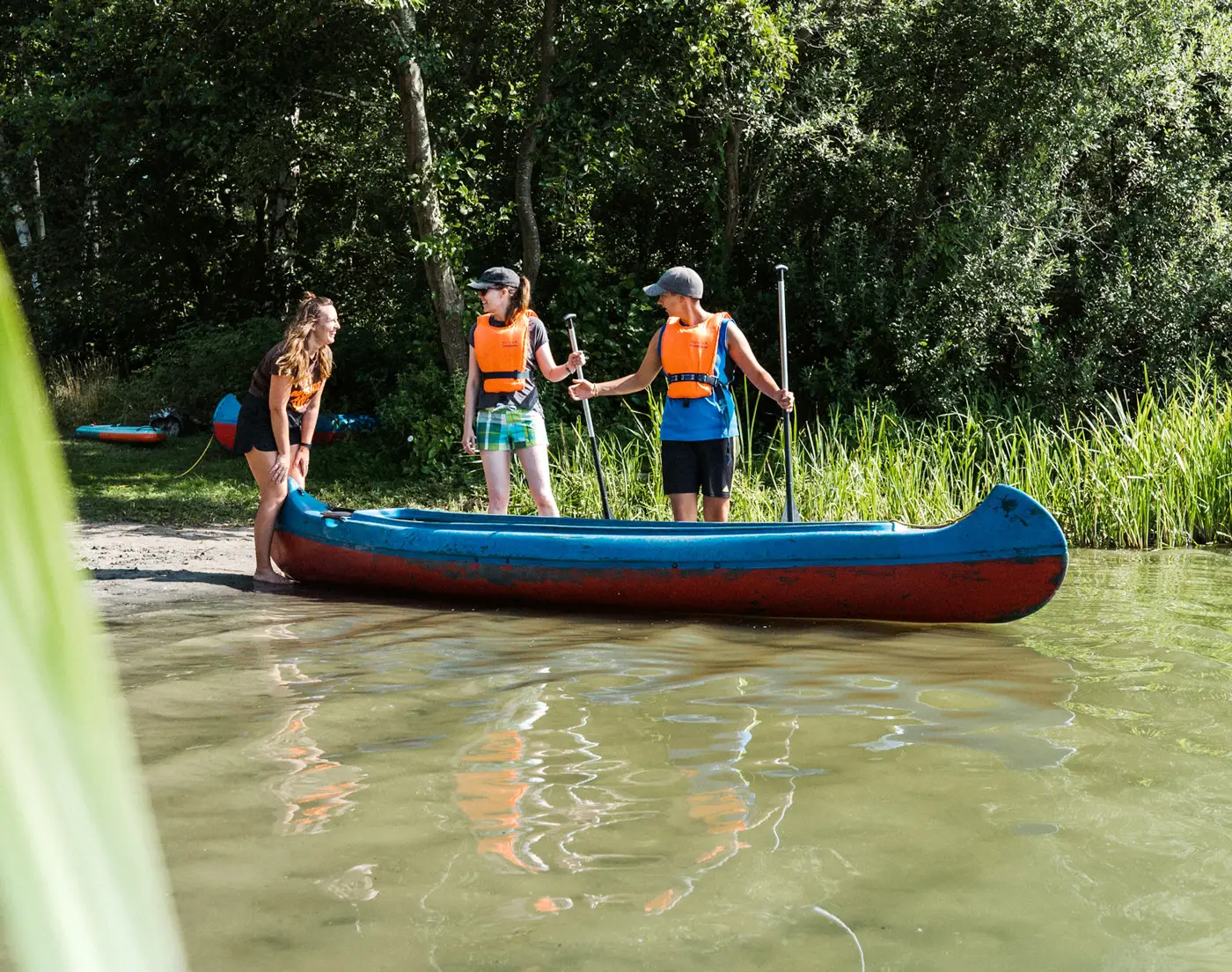 Am Seeufer hilft eine Betreuerin Teilnehmern eines Sommer-Teamcamps beim Einsteigen ins Kanu.