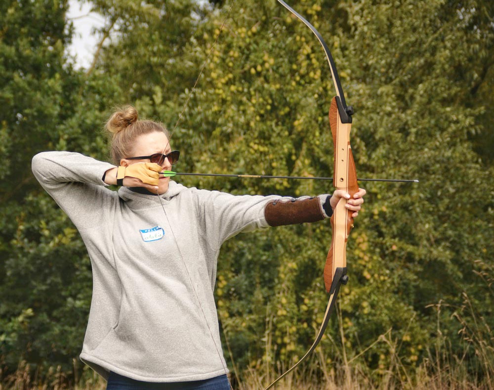Teilnehmerin spannt bei der Bogenschießen-Teamaktion den Bogen.